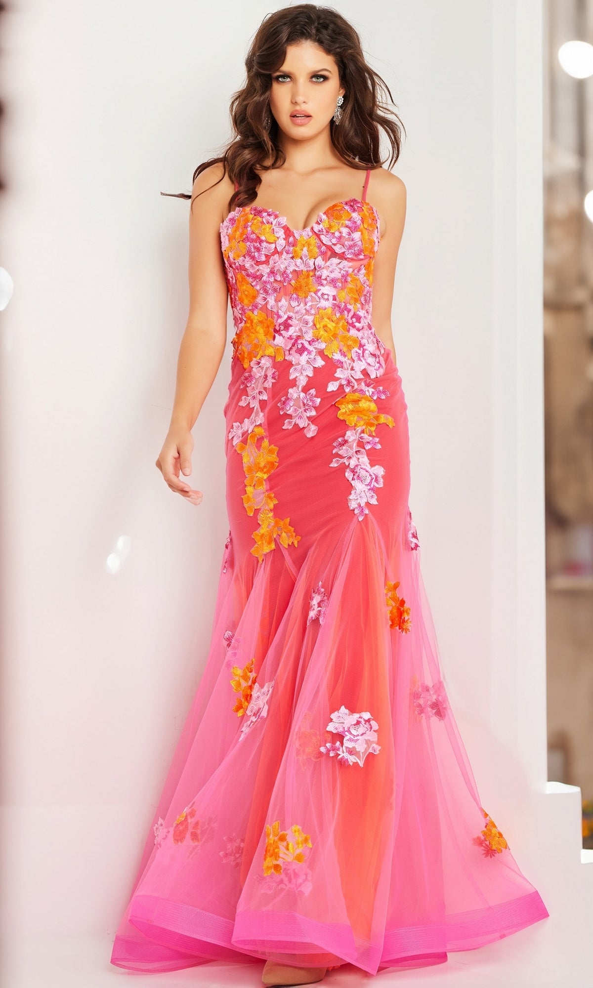 A woman stands against a light background wearing the Long Prom Dress 36843 by Jovani—a pink mermaid tulle gown featuring orange and white floral embroidery and a sweetheart neckline.